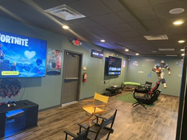The Skunkies game room: consoles on a big wall TV, gaming chairs and a painted mural.